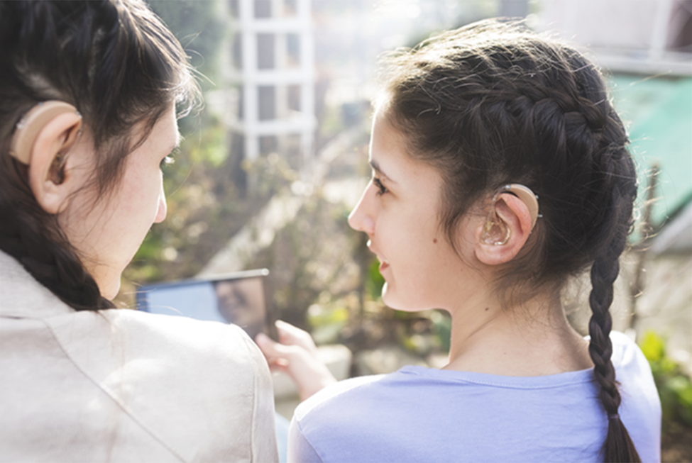 A young female student wearing a hearing aid is in close conversation with an adult female teacher
